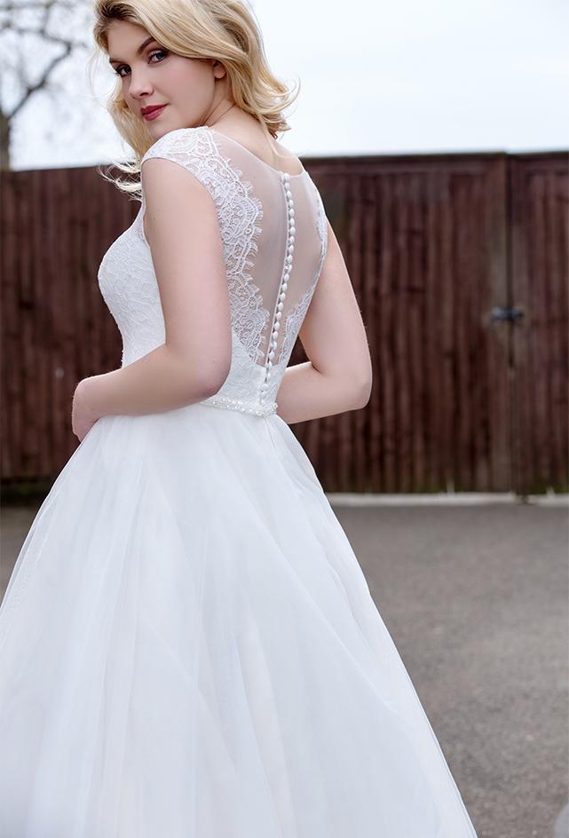 Close up of back of Tea length wedding dress with plunge lace illusion bodice and tulle skirt with pearl and bead waist detailing.